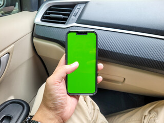 A hand holding a smartphone with a vibrant green screen inside a modern car, ideal for mobile app mockup or chroma key design in a real-life setting.