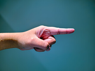 Close-up of a hand pointing with the index finger to the right against a solid blue background,...