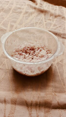 Leftover in Plastic Bowl: A plastic bowl on a tablecloth, contains remnants of a meal, viewed from an elevated perspective.
