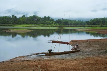 A tranquil summer landscape with fishing boats anchored on a calm river, reflecting the sky and clouds.