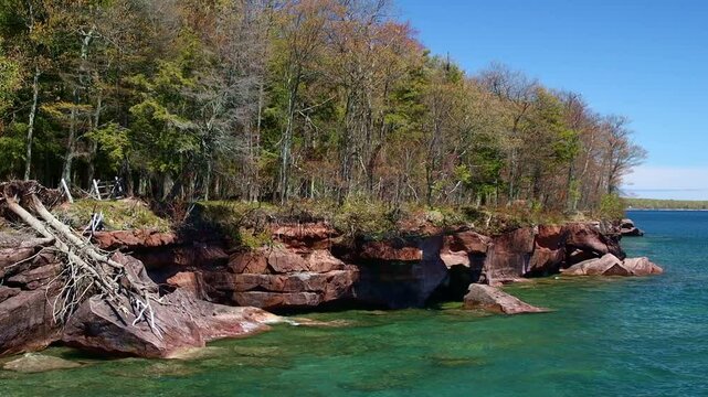 A breathtaking view of Madeline Island Lake Superior shoreline, with crystal-clear turquoise water, rocks, and vibrant spring trees, perfect for a scenic getaway
