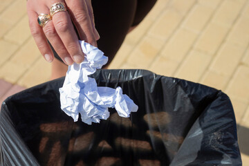 Woman throwing crumpled paper in a trash can outside