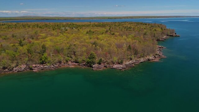 A breathtaking view of Madeline Island Lake Superior shoreline, with crystal-clear turquoise water, rocks, and vibrant spring trees, perfect for a scenic getaway