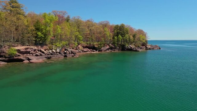 A breathtaking view of Madeline Island Lake Superior shoreline, with crystal-clear turquoise water, rocks, and vibrant spring trees, perfect for a scenic getaway