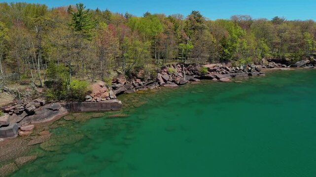 A breathtaking view of Madeline Island Lake Superior shoreline, with crystal-clear turquoise water, rocks, and vibrant spring trees, perfect for a scenic getaway