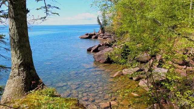 A breathtaking view of Madeline Island Lake Superior shoreline, with crystal-clear turquoise water, rocks, and vibrant spring trees, perfect for a scenic getaway