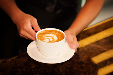 Barista skillfully pouring steamed milk into a cup of espresso, creating latte art in a cozy café during a busy morning.