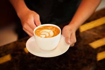 Barista skillfully pouring steamed milk into a cup of espresso, creating latte art in a cozy café during a busy morning.