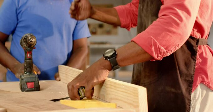 After marking plank African American mentor and apprentice drilling for screw fitting in workshop