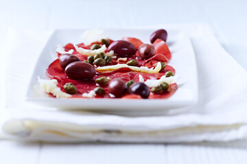 Slices of beef carpaccio with olives and capers. Close up.	