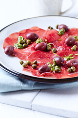 Slices of beef carpaccio with olives and capers. Close up.	