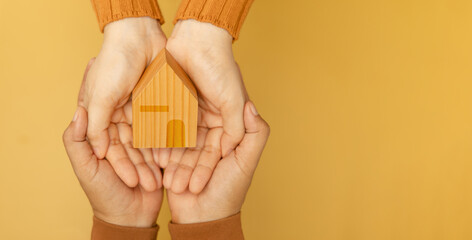Couple hands holding a yellow wooden house, symbolizing love, home, and starting a family together with warmth and unity