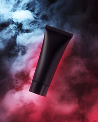 Black cream tube levitates among smoke illuminated by red light. Mystic vertical mockup of cosmetics for colored hair. Creative presentation of matte plastic packaging