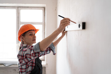 Female builder measuring wall with spirit level and marking with pencil. Renovation, construction,...