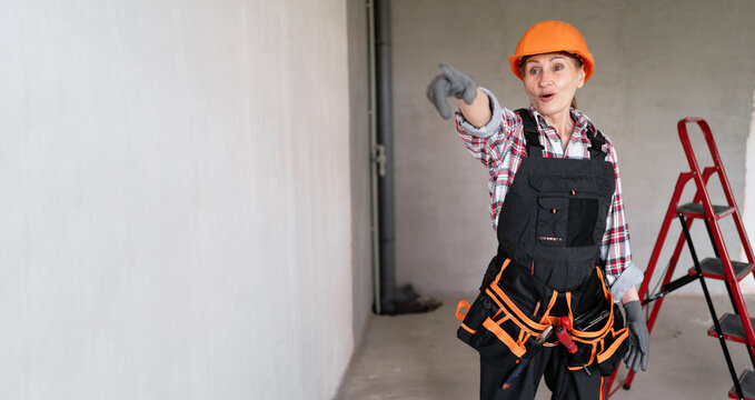 Happy builder in safety helmet and tool belt pointing at you, smiling and looking at camera. Construction concept.