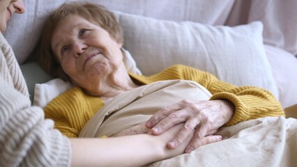 Young nurse holding hands with elderly patient lying in bed, providing comfort and care in a hospital or nursing home, fostering connection and compassion during a vulnerable moment