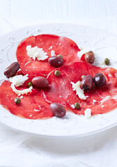 Slices of beef carpaccio with olives and capers. Close up.	