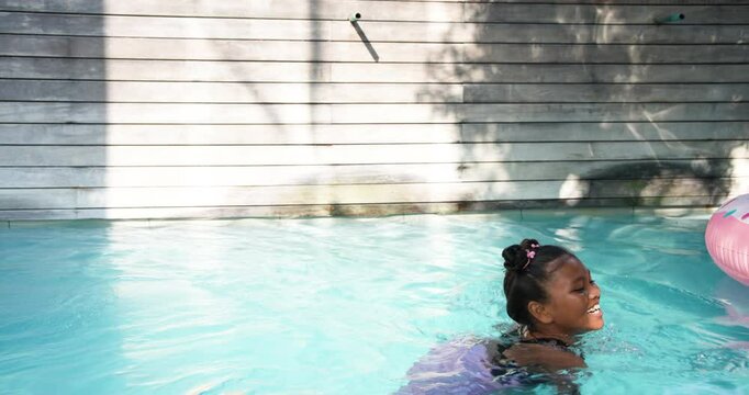 Girl in purple swimsuit kicking, stroking in pool toward coping edge, scooping pulling up, smiling