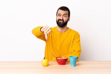 Caucasian man having breakfast in a table showing thumb down with negative expression.