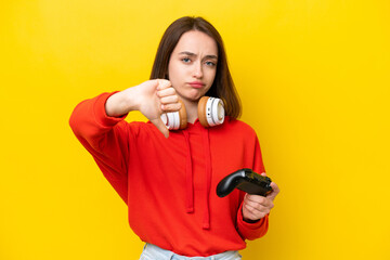 Young Ukrainian woman playing with a video game controller isolated on yellow background showing...