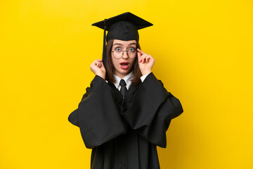 Young university graduate Ukrainian woman isolated on yellow background with glasses and surprised