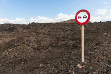 A road sign stands on rugged, dark volcanic soil in Lanzarote, Canary Islands, Spain. The sign...