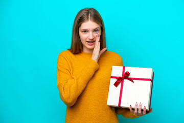 Teenager Russian girl holding a gift isolated on blue background whispering something