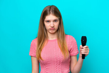 Singer Russian girl picking up a microphone isolated on blue background with sad expression