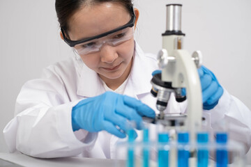 A focused young scientist examines samples under a microscope in a laboratory setting, wearing...
