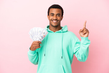 Young man taking a lot of money over isolated pink background pointing up a great idea