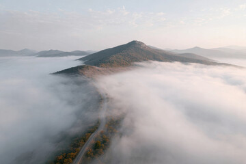 aerial view of mystical mountains shrouded in morning fog highlighting solitary path winding through landscape