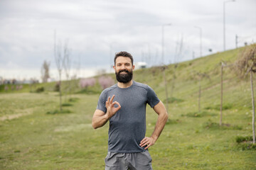 Fototapeta premium Portrait of smiling sportsman standing on a meadow and gesturing okay at the camera.