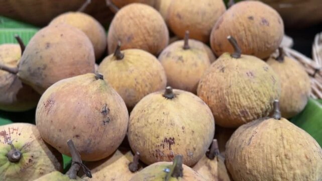 Ripe santol fruits in basket on banana leaves at tropical fruit market.
