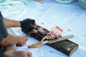 A person cutting sacrificial meat using a meat knife with a wooden base during Eid al-Adha