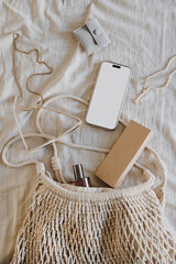 Smartphone and Accessories in Natural Mesh Bag on Neutral Fabric Background