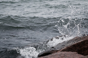 Close-up of splash of a small wave crashing on rocks on a cloudy day.
