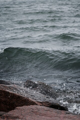 Close-up of splash of a small wave crashing on rocks on a cloudy day.