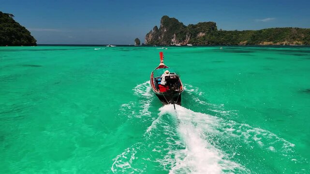 Wooden longtail boat gliding across turquoise waters, cutting white wake near verdant phi phi islands tropical landscape, Phi Phi island, Phuket, Thailand.