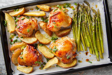 Baked chicken thighs in honey mustard sauce with potato wedges and asparagus close-up on a baking...