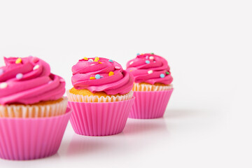 Three pink frosted cupcakes with colorful sprinkles on white background