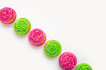 Vibrant cupcakes with colorful frostings and sprinkles arranged linearly on white background