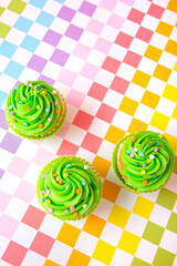 Green frosted cupcakes with colorful sprinkles on checkerboard background, top view