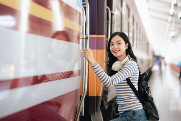 Asian woman sitting at a railroad station with backpack, using mobile phone and laptop, waiting for train, enjoying travel lifestyle.