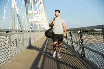 A man walks across a bridge carrying a sports bag, symbolizing an active lifestyle and dedication to fitness and personal health.
