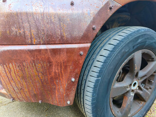A car with a black tire and a black rim has a rusty exterior. The car appears to be old and has been exposed to the elements for a long time
