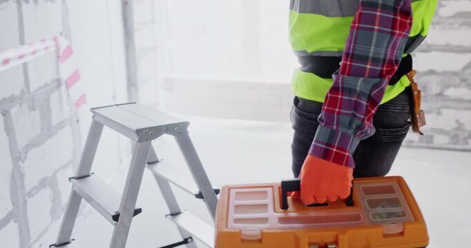 Specialist arrives at renovation site and opens special toolbox. Builder prepares to start work fulfillment in spacious apartment hall using specialized equipment