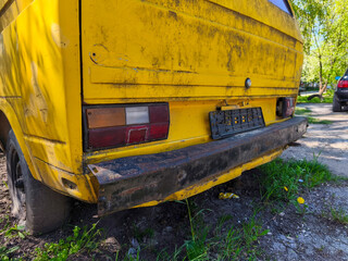 A yellow old truck with a black tail light. The back of the truck is rusted and dirty