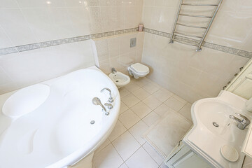 bright, tiled bathroom with a jacuzzi tub, toilet, bidet and a towel rack