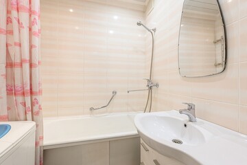 bright bathroom features peachy tile walls, a white bathtub with a safety bar, a white sink vanity,...