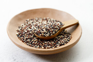 Mix of white, black and red quinoa seeds in wooden spoon.
